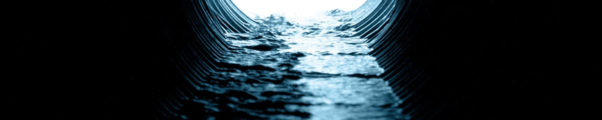 View down the inside of a corrugated drain pipe with water flowing through it